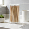 A clear plastic package filled with numerous wooden cotton swabs lying on a white countertop.