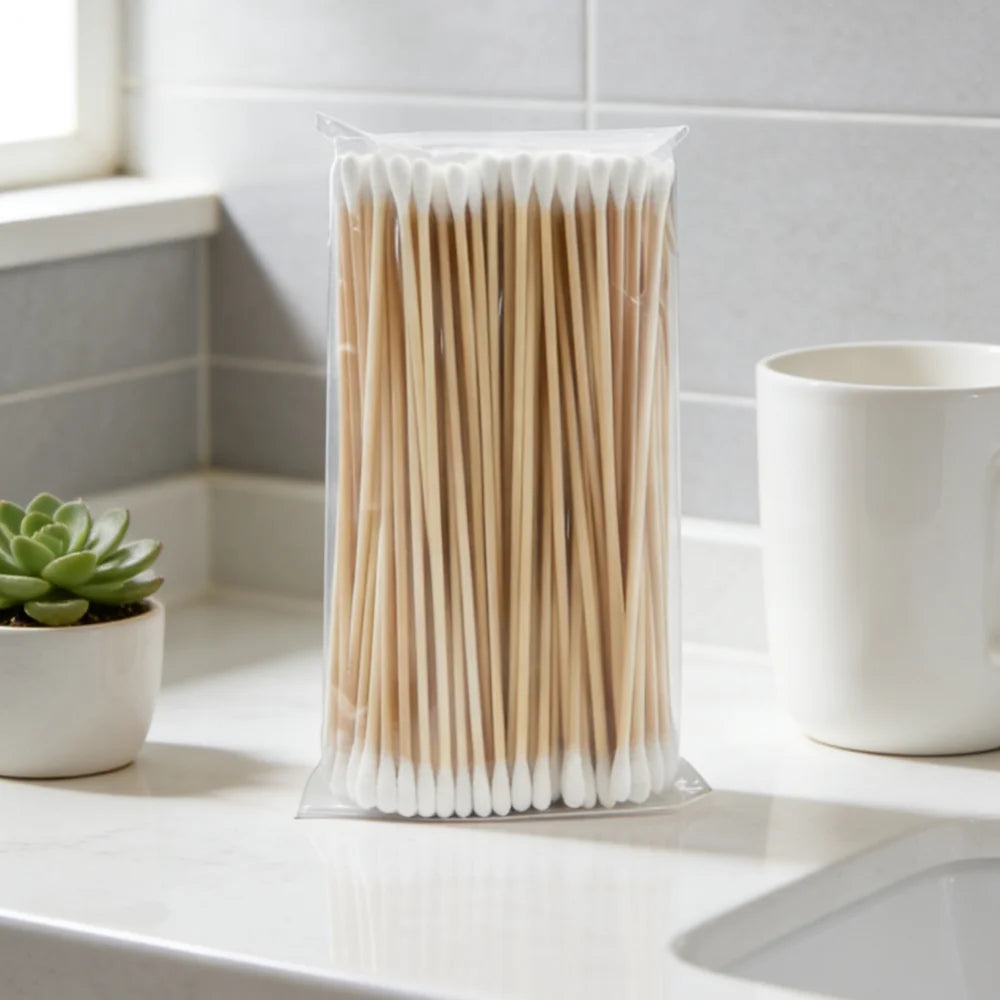 A clear plastic package filled with numerous wooden cotton swabs lying on a white countertop.
