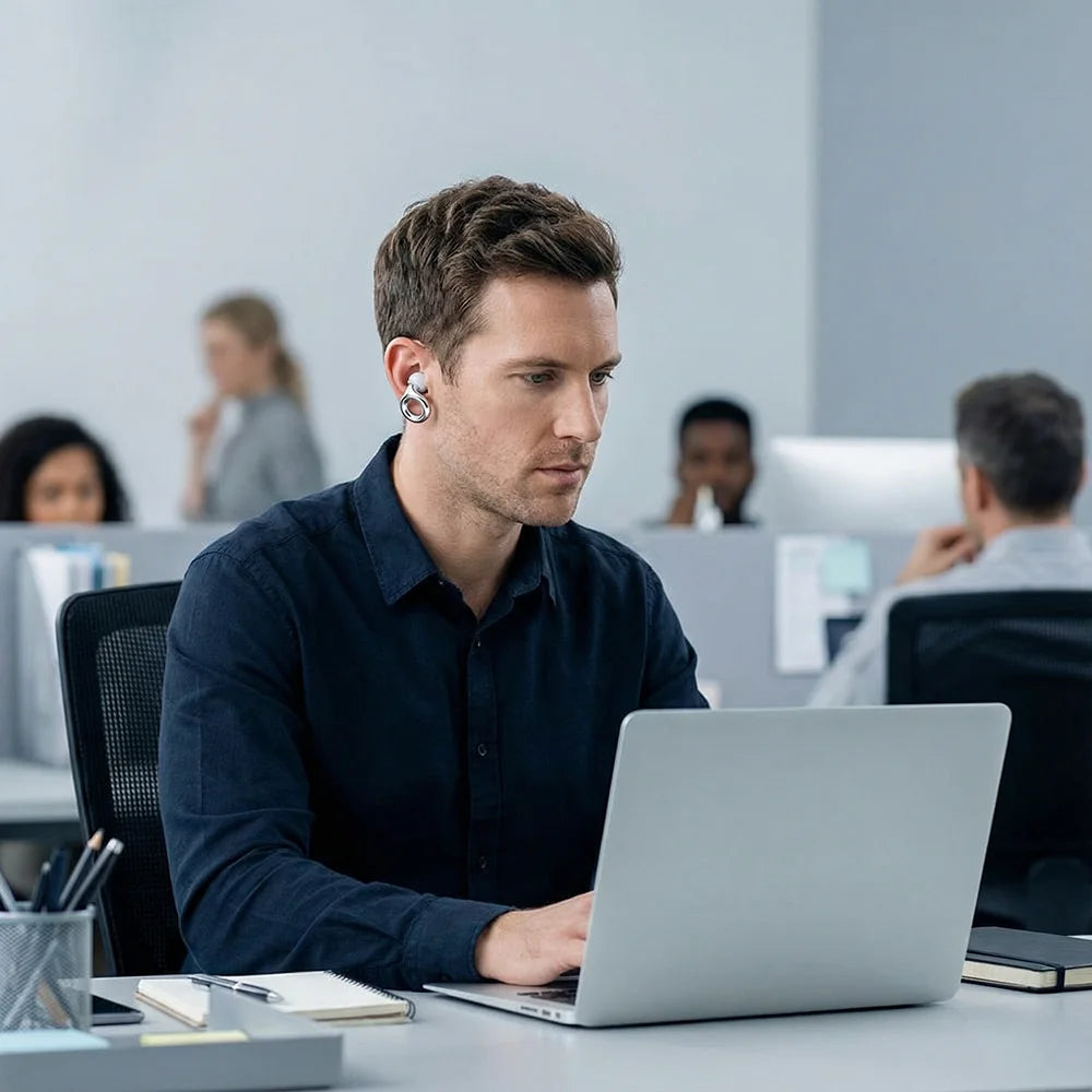 A man working on a laptop in an office setting, wearing silicone noise-cancelling earplugs.