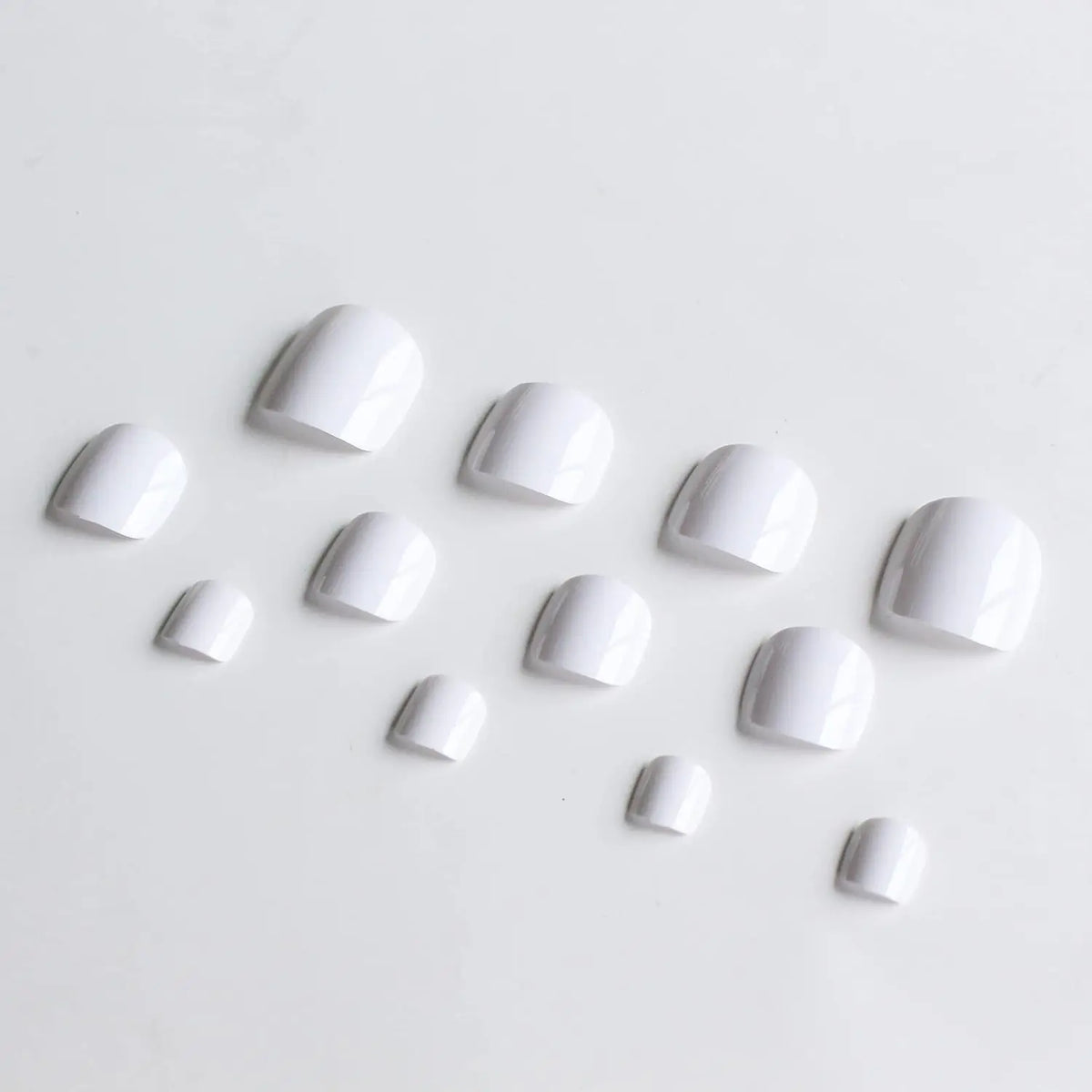 A collection of white reusable press-on acrylic false nails scattered on a white background.