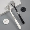 A white reusable tongue cleaner brush with a black handle and a separate cleaning disc is shown on a gray surface.