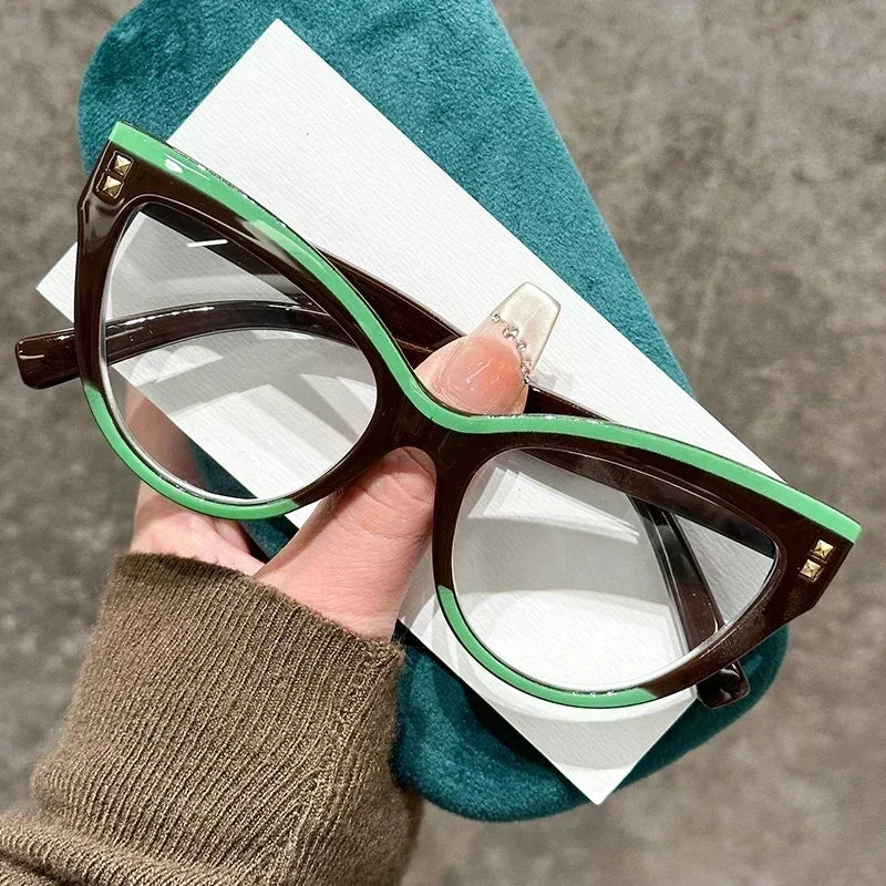 Une main tient une paire de lunettes à œil de chat marron et vert posées sur un tissu bleu sarcelle.
