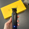 A hand holds a black cordless electric hair clipper against a yellow box.