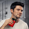 A man holds a red electric foil shaver trimmer near his jawline in a well-lit indoor setting.