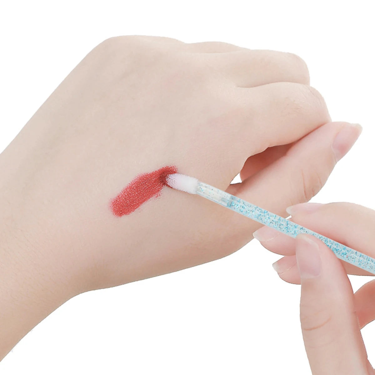 A hand is using a thin brush to apply red pigment onto the skin for lip or eyelash extensions.