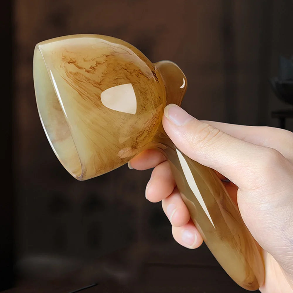 A hand holds a smooth, amber-colored resin gua sha tool, showing its polished surface and ergonomic handle.
