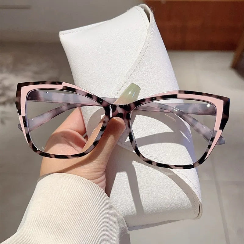 Une paire de lunettes à monture œil de chat élégantes à motif écaille de tortue, tenues au-dessus d'une étui en cuir blanc.