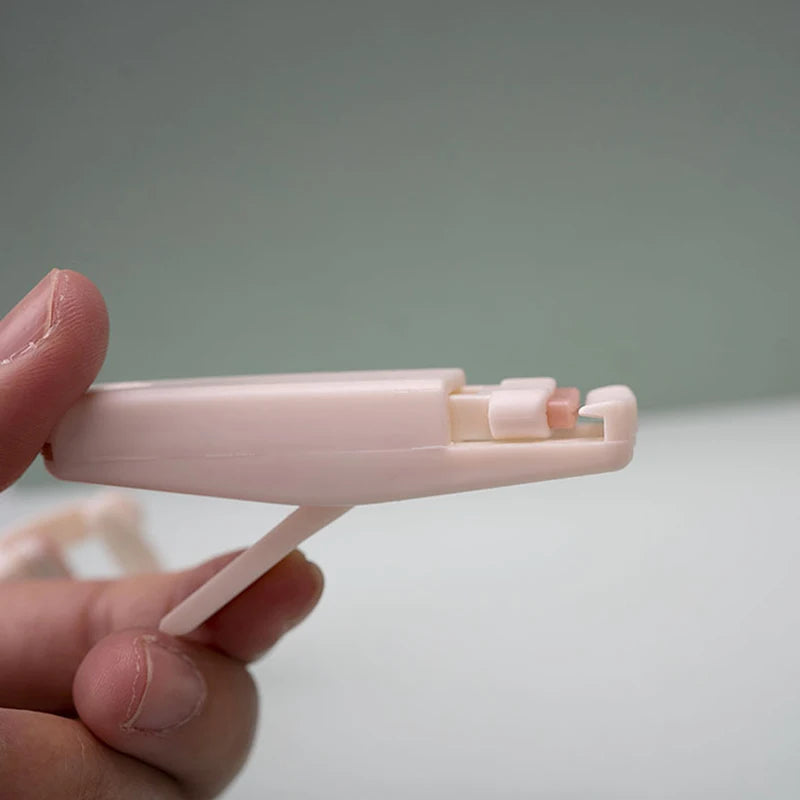 A hand holds a pink plastic cartoon mini eyelash curler against a light gray background.