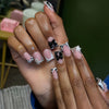 A close-up of a hand displaying nude pink press-on nails decorated with leopard print and silver 3D charms.
