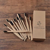 Une boîte en carton contenant dix brosses à dents en bambou posées sur une surface en bois.