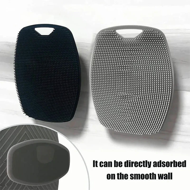 A black silicone body scrubber and a gray textured silicone scrubber are shown next to a smooth wall surface.