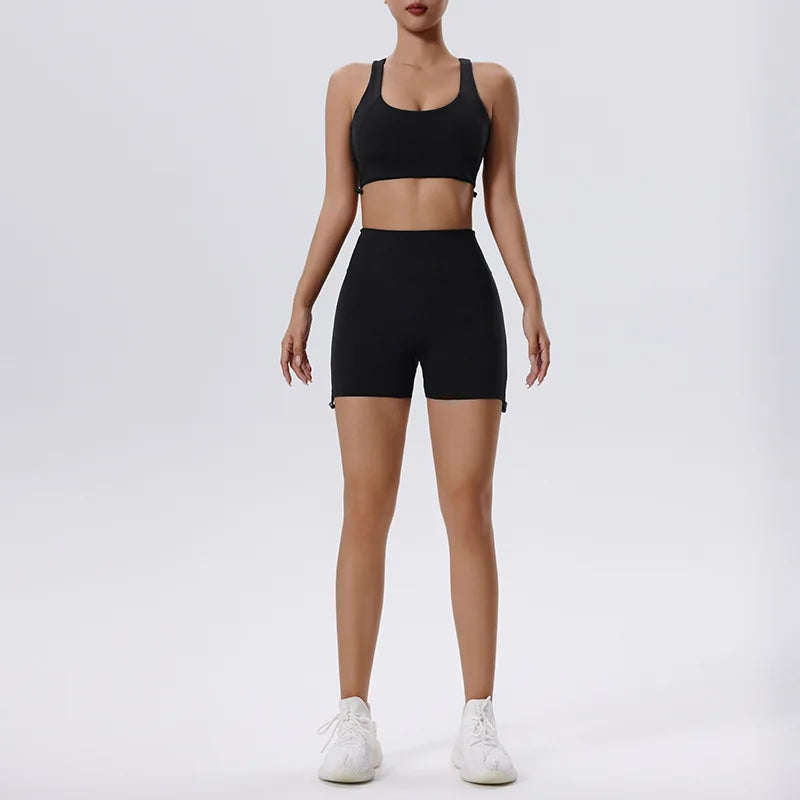 Una mujer modela un conjunto deportivo de yoga y gimnasio negro, compuesto por un top deportivo y shorts.