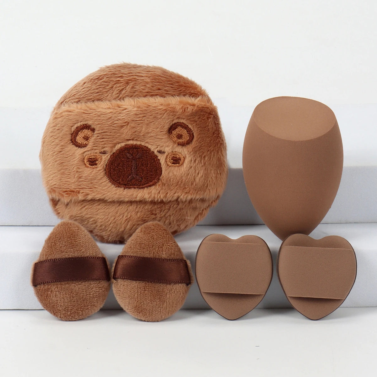 Un set de trois éponges de poudre rondes, couleur daim, avec un dessus texturé et duveteux.