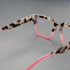 Un par de gafas de lectura cuadradas con montura de estampado de leopardo y temples rosas contra un fondo gris.