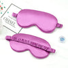 Un masque de sommeil imitation soie rose en forme de coussin incurvé, à côté d'un petit récipient de perles.