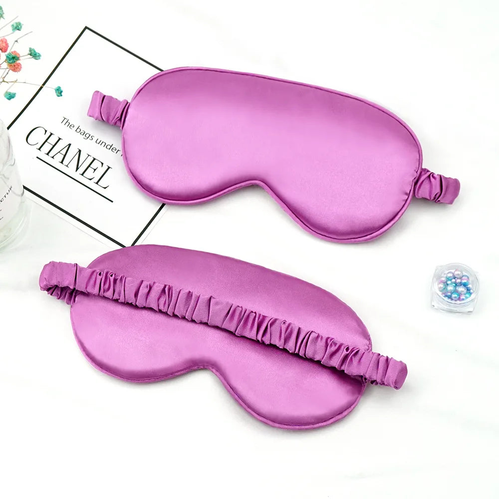 Un masque de sommeil imitation soie rose en forme de coussin incurvé, à côté d'un petit récipient de perles.