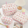 A pink quilted cotton makeup bag with a floral pattern is shown next to a lamp and a makeup brush.