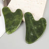 A smooth, translucent green jade gua sha tool resting on a light beige stone.
