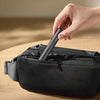 A hand is using a black electric nose and eyebrow hair trimmer inside a black zippered pouch.