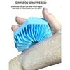 A hand holds a blue silicone exfoliating shower scrub brush against light skin.
