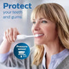 A woman is using a white electric toothbrush with a pressure sensor to clean her teeth.