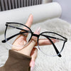 Une main tient une paire de lunettes à monture noire de style œil de chat avec des verres clairs sur un fond blanc et duveteu