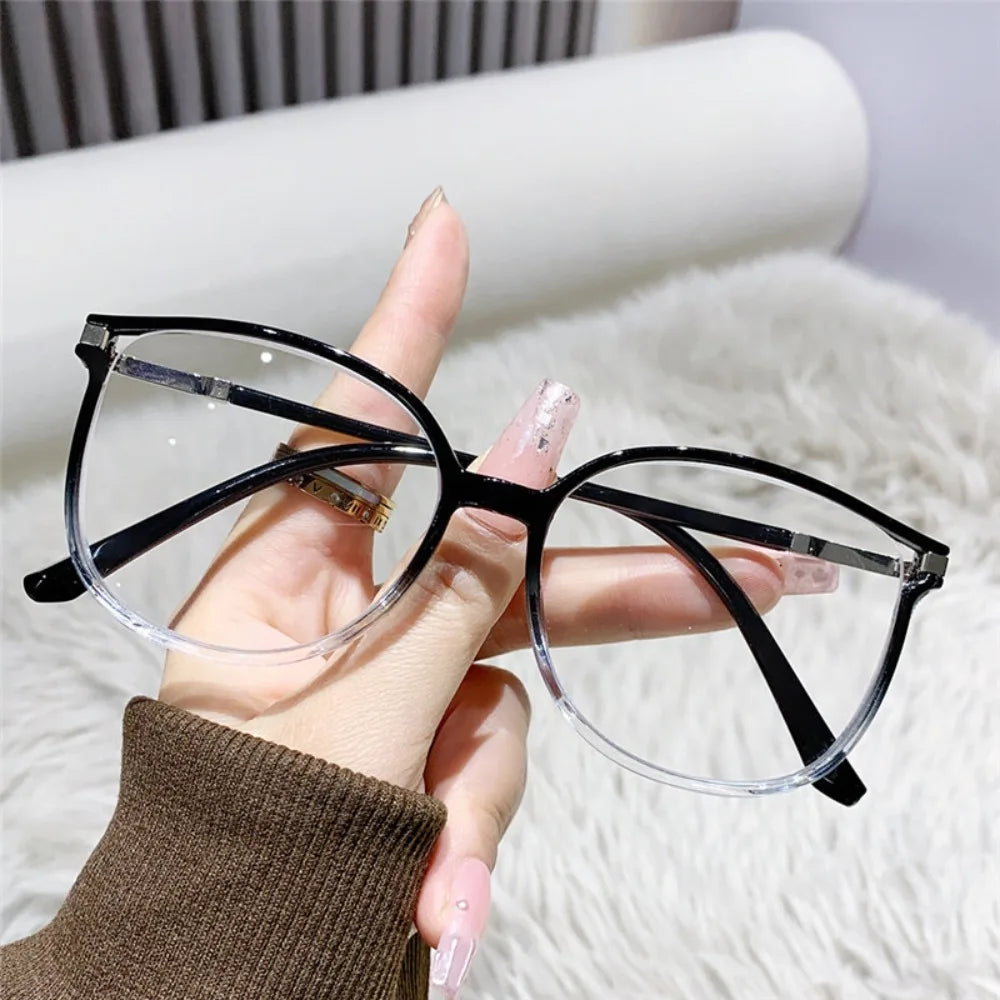 Une main tient une paire de lunettes à monture noire de style œil de chat avec des verres clairs sur un fond blanc et duveteu