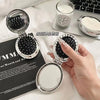 A silver folding massage comb with a mirror is shown next to a notebook and a laptop.