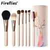 A set of professional makeup brushes in a beige cylindrical case with artistic designs.