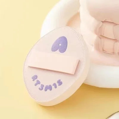 Pinceau cosmétique rose flocké avec un cœur violet sur fond jaune clair.
