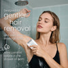 A woman is using a hair removal device to gently remove hair from her arm while in the shower or bath.