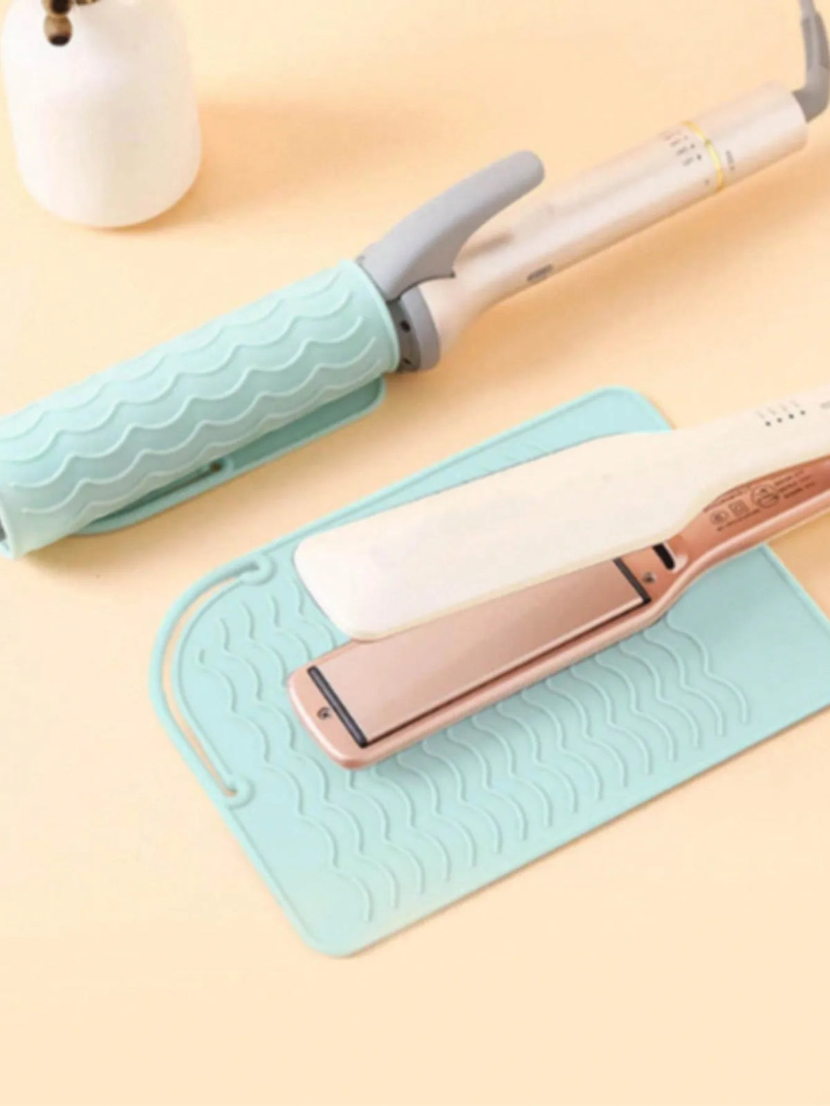 A silicone heat resistant mat is shown under a pair of silver hair styling tools.