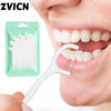 A hand holds a white dental floss pick against a person's mouth, with a green pouch of the same picks visible.