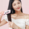 A woman is using a pink automatic hair ends trimmer on her long black hair.