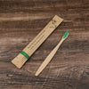 A bamboo toothbrush packaged on natural kraft paper, lying diagonally on a dark wooden surface.