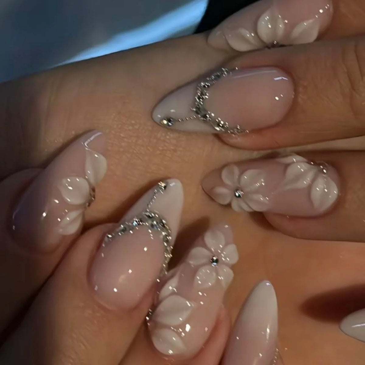 Gros plan d'une main montrant des ongles press-on à noisette française roses avec de délicats accents floraux.