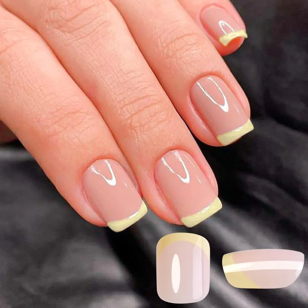 A hand displays a set of press-on nails featuring soft pink and pale yellow accents.