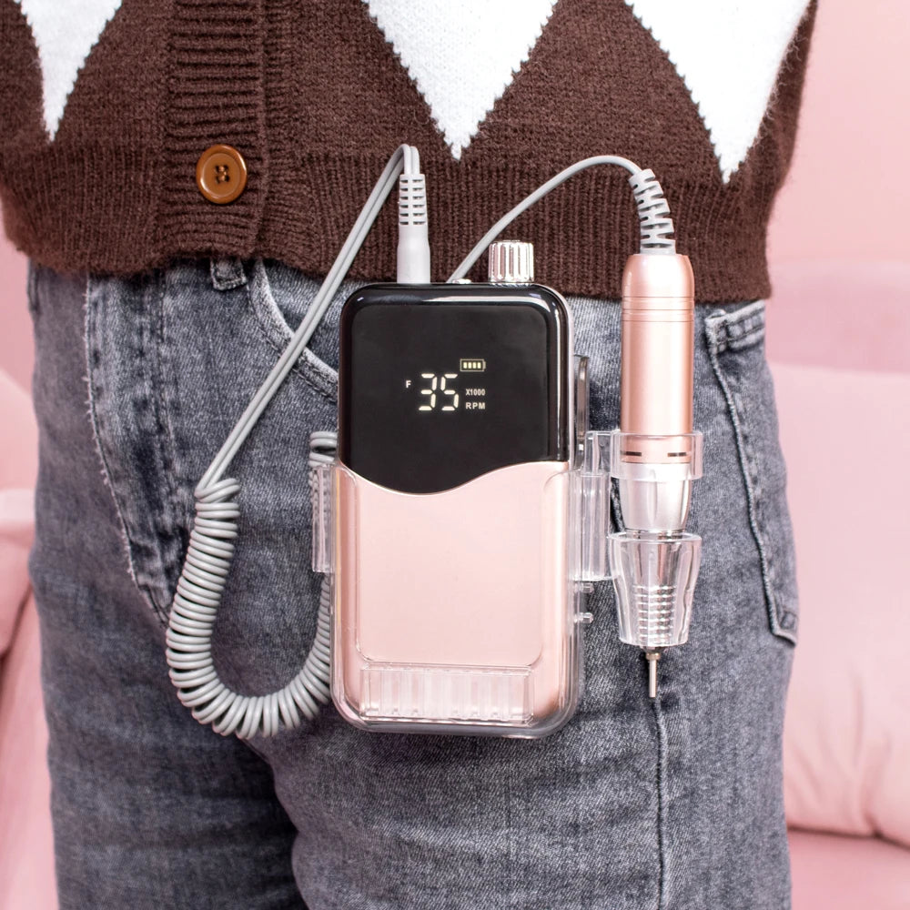 A cordless rechargeable nail drill with a pink body and white cord is shown attached to jeans.