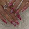 A hand displays a set of 24 press-on almond nails featuring pink and white floral and butterfly designs.