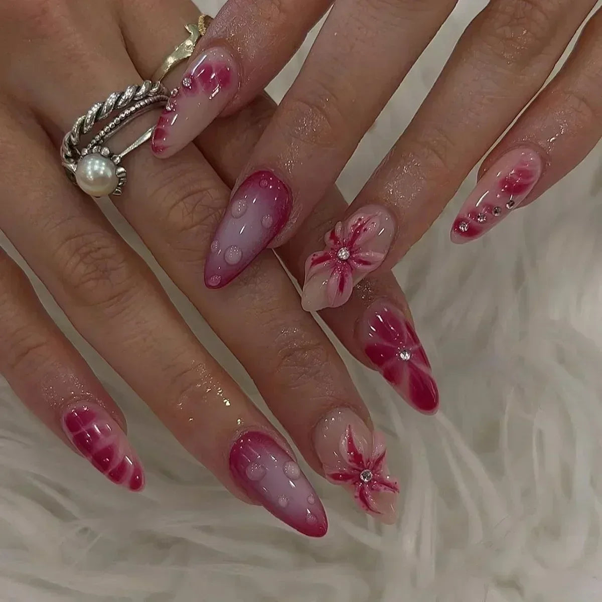 A hand displays a set of 24 press-on almond nails featuring pink and white floral and butterfly designs.