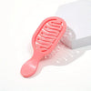 A pink mini travel hair brush is shown next to its white packaging box.