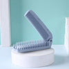 A light blue portable folding hairbrush with anti-static bristles resting on a white circular base.