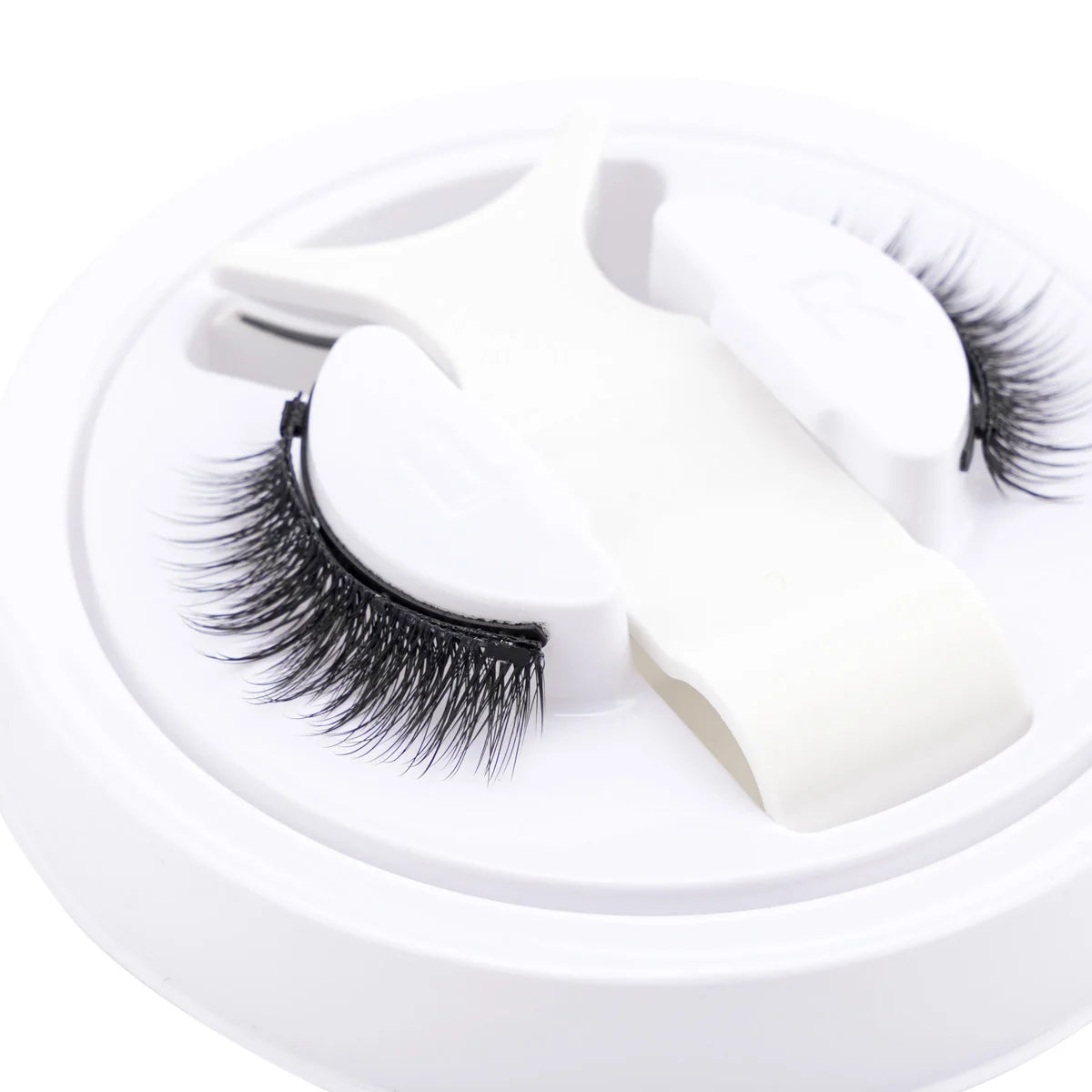 Un ensemble de faux cils magnétiques réutilisables blancs avec pinces, présenté sur un fond blanc circulaire.