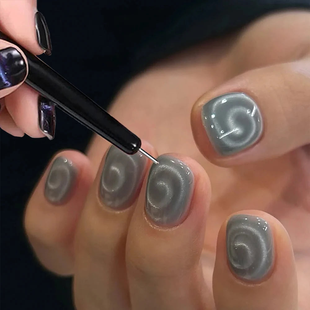 Une main utilise un outil fin pour appliquer un design de ongles gris et argenté tourbillonnant sur une ongle.