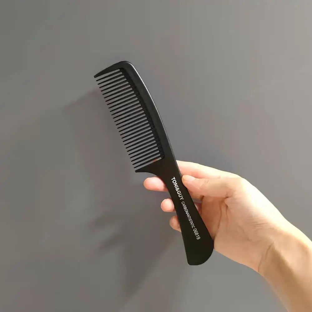 A hand holds a black anti-static carbon hair comb with fine teeth against a gray background.