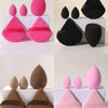 A set of five makeup sponges in various shades of pink, black, and brown are displayed on white boxes.