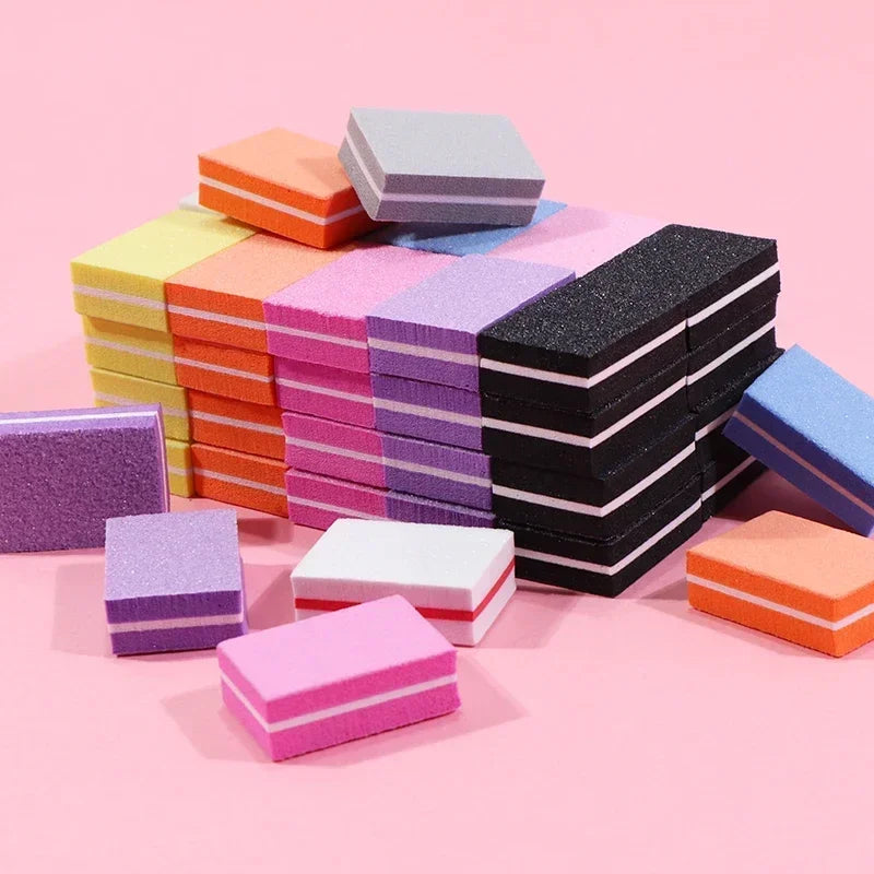 A collection of colorful, multi-sided nail and cuticle buffing files stacked on a pink surface.