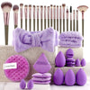 A collection of purple makeup brushes, sponges, and tools arranged on a light-colored surface.