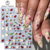 Close-up of a hand displaying floral and insect nail art stickers on fingernails.
