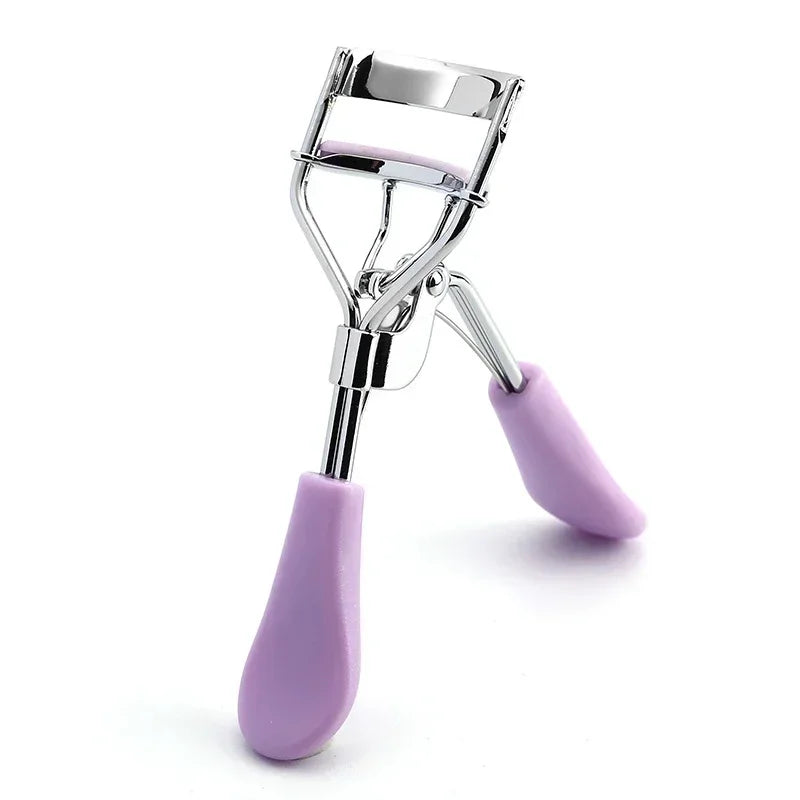 A silver professional eyelash curler with purple silicone grips shown against a white background.